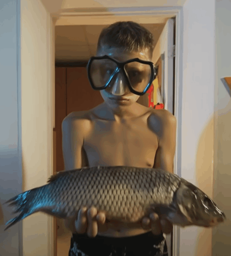 a shirtless boy wearing goggles is holding a fish