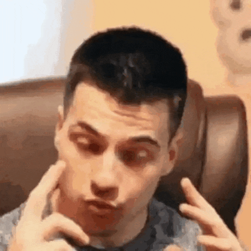 a man is sitting on a couch making a funny face with his hands on his face .