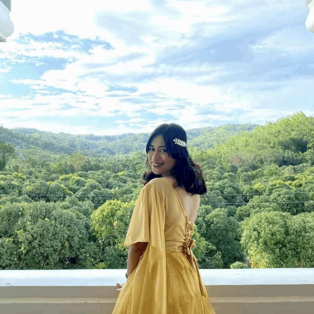 a woman in a yellow dress is standing in front of a forest