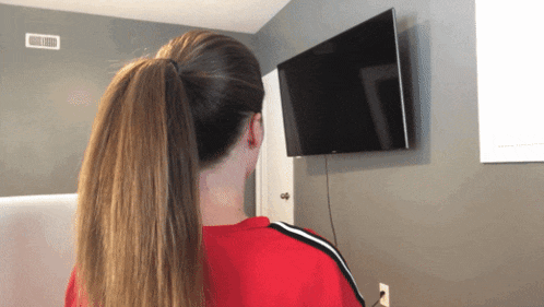 a woman in a red shirt looks at a flat screen tv mounted on a wall