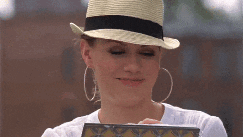 a woman wearing a straw hat and hoop earrings is smiling while writing on a clipboard