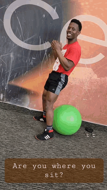 a man in a red shirt is standing on a green exercise ball with the words are you where you sit below him