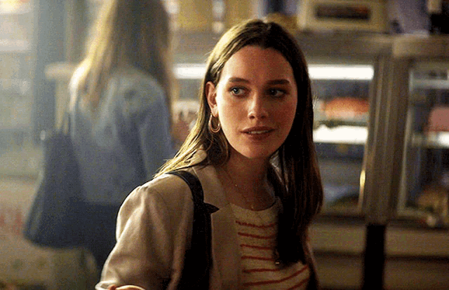 a woman in a striped shirt and a white jacket stands in a dark room