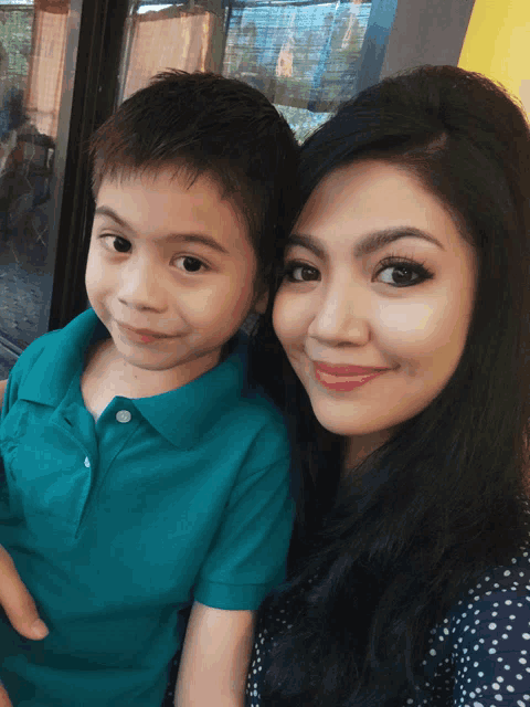 a woman holds a young boy in her arms and they both smile for the camera