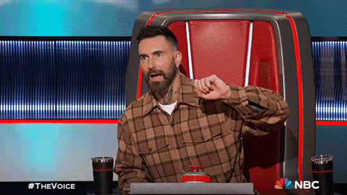 a man in a plaid shirt is sitting in a chair with a nbc logo on it