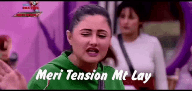 a woman in a green hoodie is standing in front of a purple background and says meri tension mt lay .