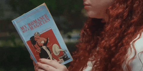 a woman with red hair is holding a book titled my romance with a magician