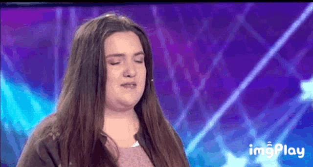a woman with long hair is crying on a stage in front of a purple background