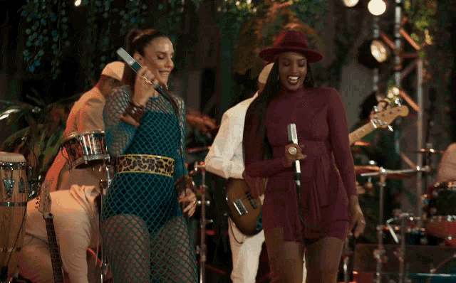 a woman singing into a microphone next to another woman in a red hat