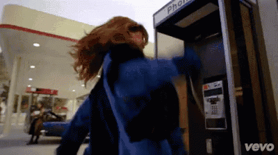 a woman is standing in front of a pay phone booth that says vevo