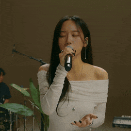 a woman singing into a microphone with a keyboard in the background
