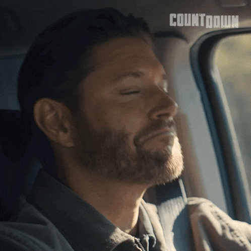 a man with a beard is sitting in a car with his eyes closed and the word countdown behind him