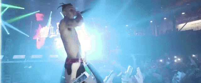 a man without a shirt is singing into a microphone on stage .