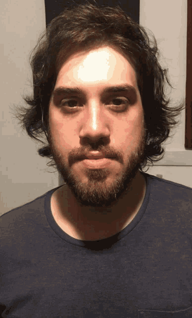 a man with a beard and long hair looks at the camera