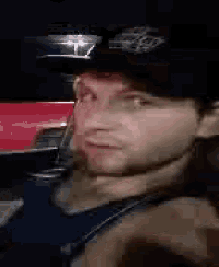 a man wearing a hat and a blue tank top is sitting in a car .