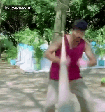 a man in a pink tank top is standing next to a tree .