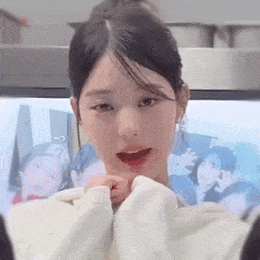 a close up of a woman wearing a white sweater making a heart shape with her hands .