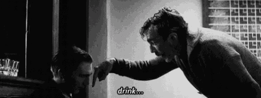 a man is pointing at another man who is drinking .