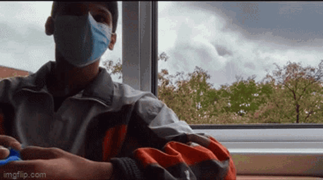 a man wearing a face mask is sitting in front of a window ..