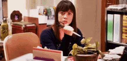 a woman is sitting at a desk holding a pair of scissors in front of a potted plant .