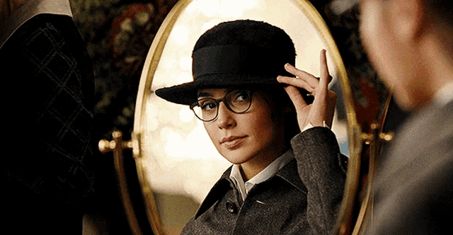 a woman wearing glasses and a hat is looking in a mirror