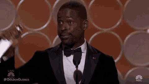 a man in a suit and bow tie is giving a speech at a podium .