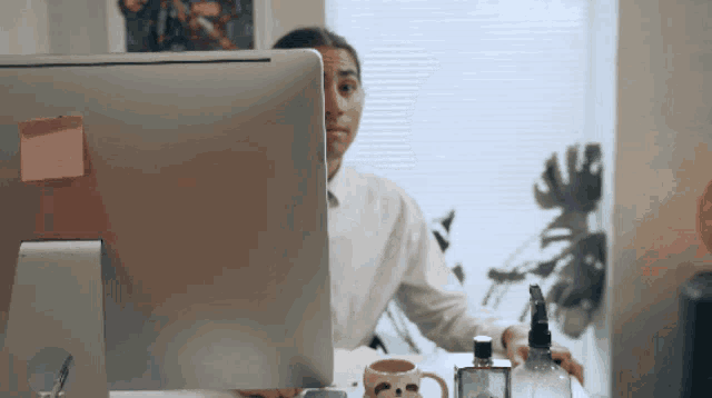 a woman sits at a desk in front of a computer with a pink sticky note on it