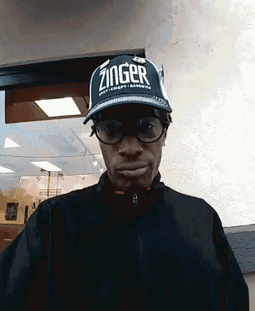 a man wearing a zinger hat and glasses looks at the camera