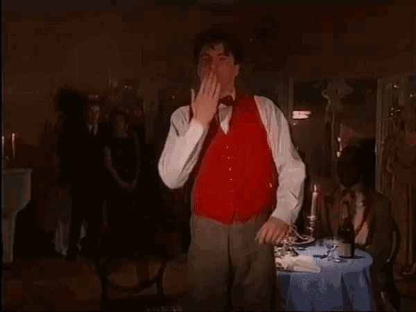 a man in a red vest is standing in front of a table with a bottle of wine on it
