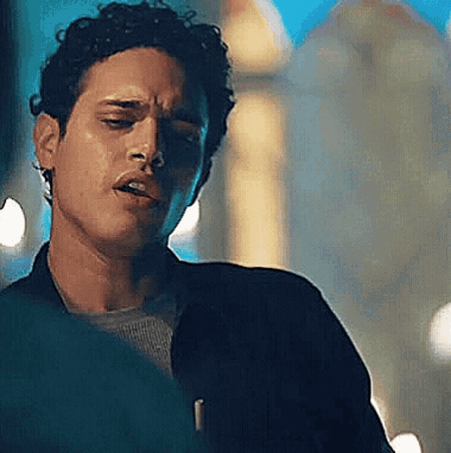 a man with curly hair is standing in front of a building with his eyes closed and his mouth open .