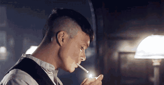 a man is lighting a cigarette in a dark room with a lamp .