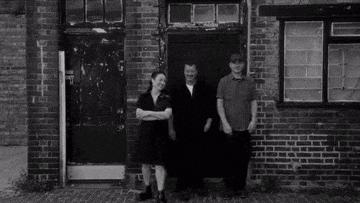 a black and white photo of a group of people standing next to each other in front of a brick wall .