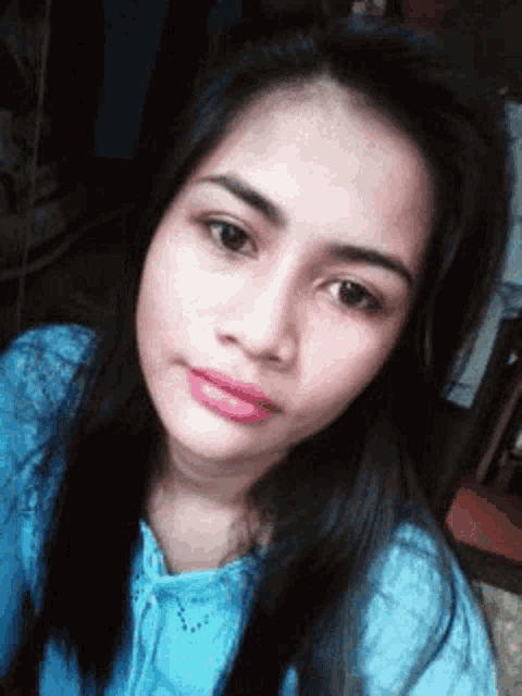 a woman with long black hair is wearing a blue shirt and taking a selfie