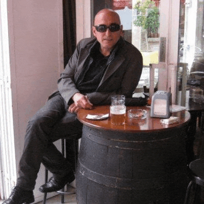 a man wearing sunglasses is sitting at a table with a glass of beer and a cigarette .