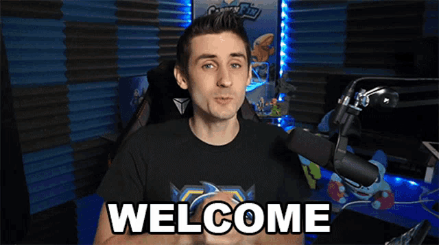 a man standing in front of a microphone with the words welcome on his chest