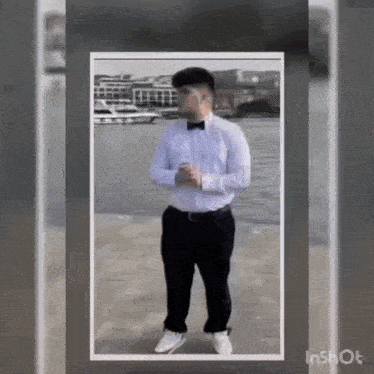 a man in a white shirt and black pants is standing on a sidewalk in front of a body of water .