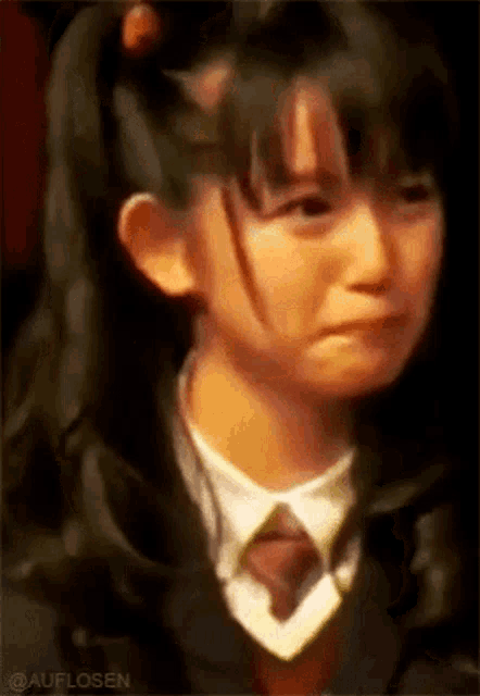 a young girl in a school uniform and tie is crying