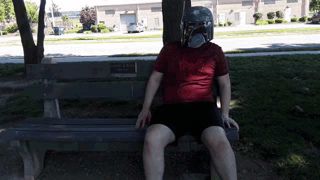 a man wearing a bounty hunter mask sits on a bench