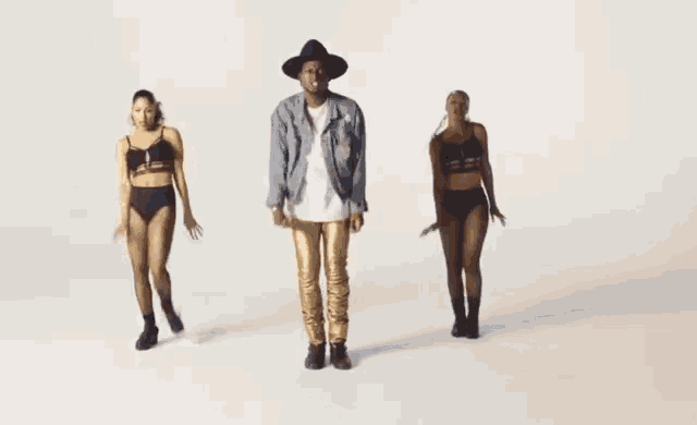 a man in a hat is dancing with two women in underwear .