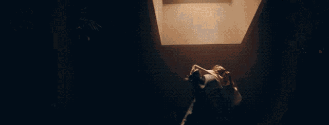 a person standing in a dark room with a light shining through the ceiling