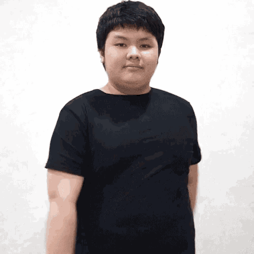 a young man wearing a black t-shirt stands in front of a white wall .