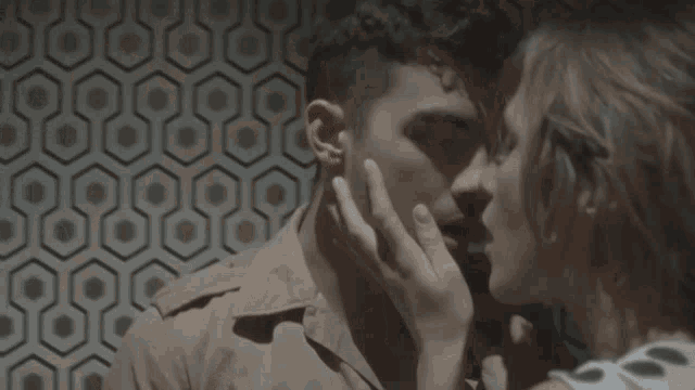 a man and a woman are kissing in front of a patterned wallpaper