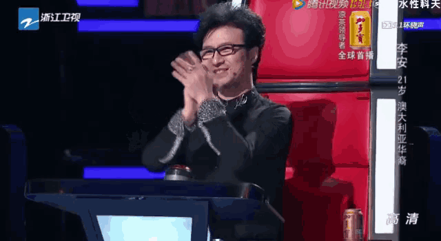 a man wearing glasses is clapping his hands in front of a sign that says ' a ' on it