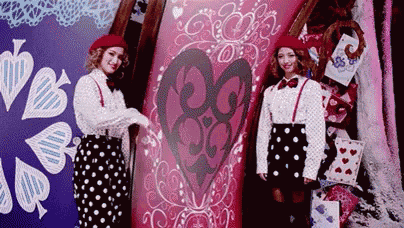 two women in polka dot skirts are standing next to each other in front of a pink wall with a heart on it .