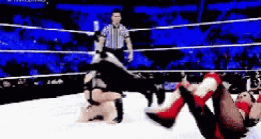 a wrestler is doing a handstand in a wrestling ring with a referee watching .