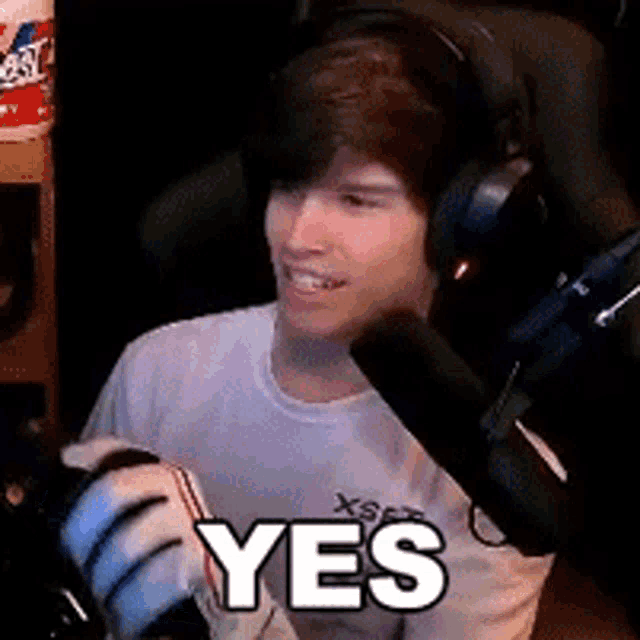 a young man wearing headphones is sitting in front of a microphone and saying yes .