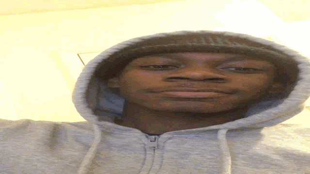 a man wearing a grey hoodie and a black hat looks at the camera