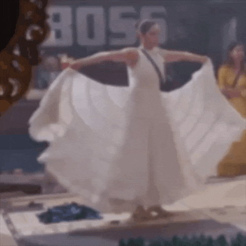 a woman in a white dress is dancing on a stage in front of a sign that says boss .
