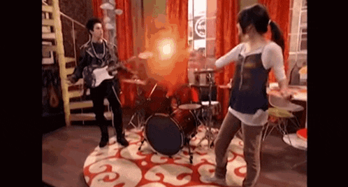 a man is playing a guitar and a woman is dancing in front of a drum set in a room .