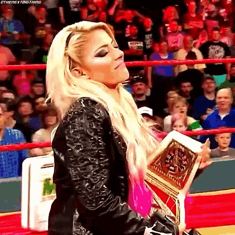 a woman is standing in a wrestling ring holding a championship belt .